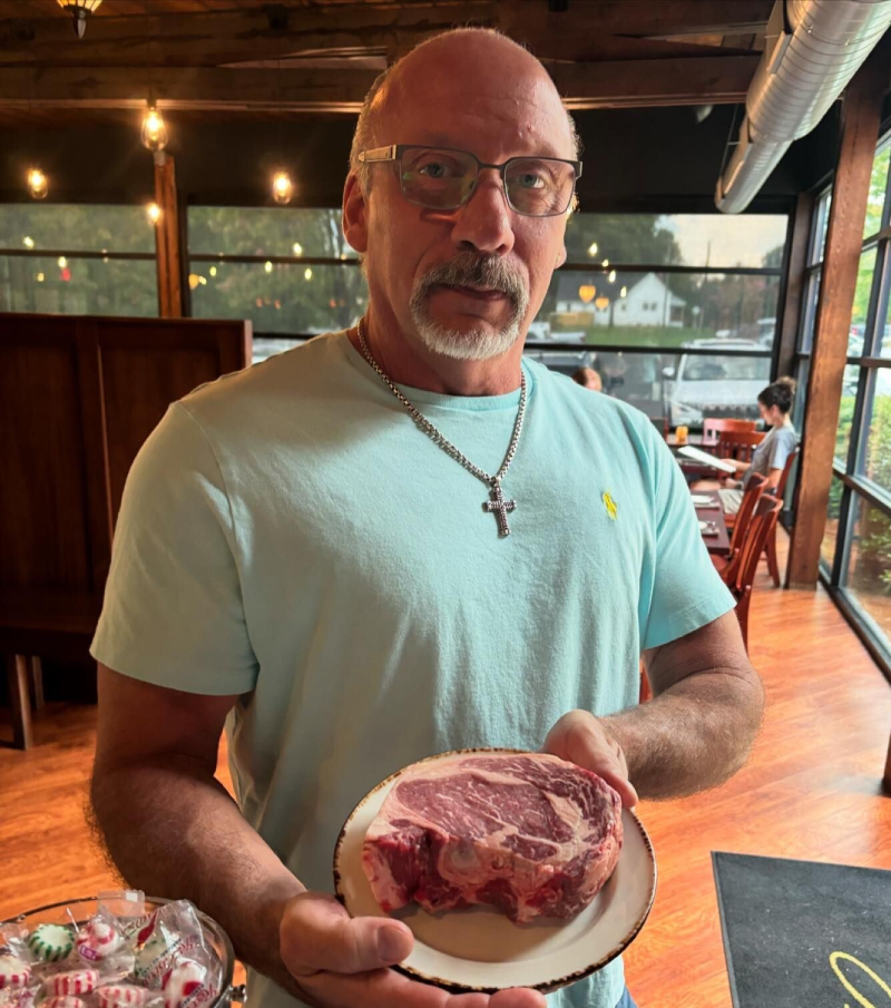 John with holding a plate with a large uncooked steak